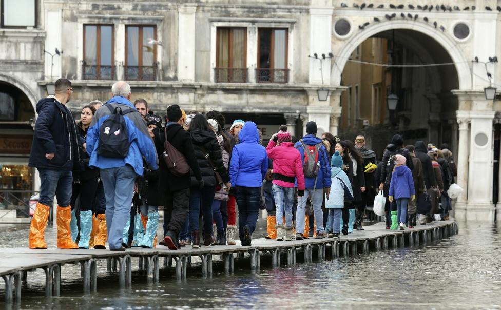 tourists walk on raised platforms above flood waters during a period of seasonal high water and on the first day of carnival, in venice