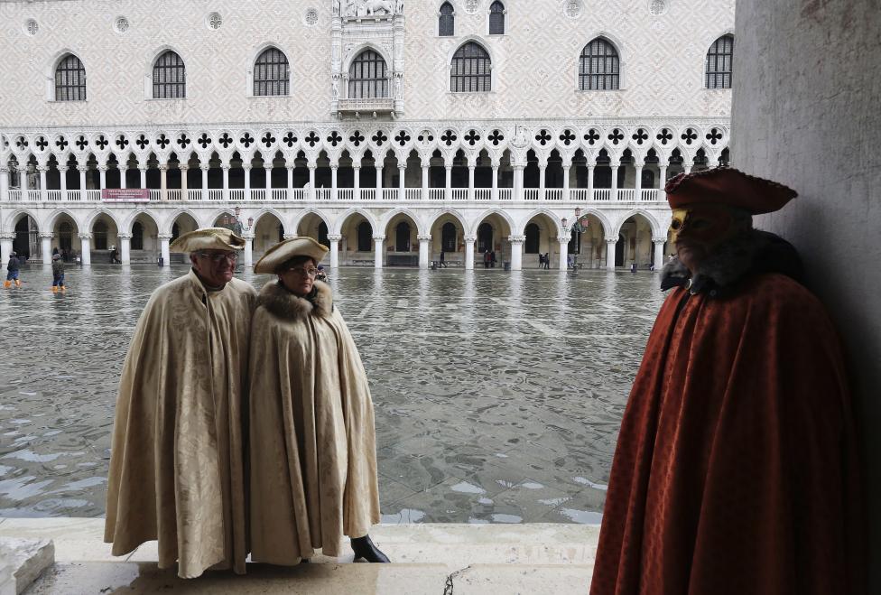 masked revellers pose along the flooded st. mark's square during a period of seasonal high water and on the first day of carnival, in venice