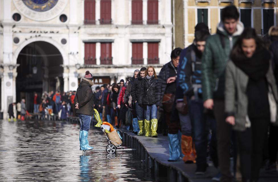 tourists walk on raised platforms above flood waters in st. mark's square during a period of seasonal high water in venice