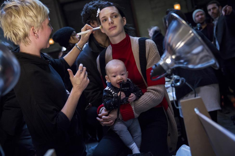 A model holds a baby while being made-up backstage before the Vera Wang Fall/Winter 2015 collection show at New York Fashion Week