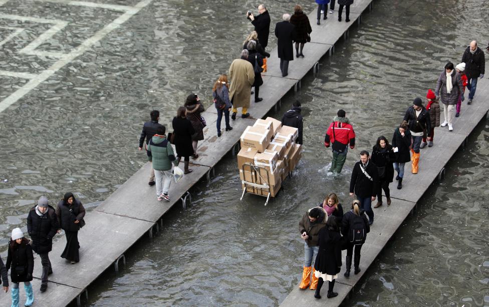 tourists walk on raised platforms above flood waters in st. mark's square during a period of seasonal high water in venice