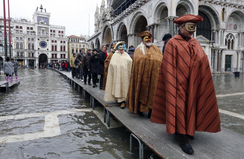 masked revellers walk on raised platforms above flood waters during a period of seasonal high water and on the first day of carnival, in venice