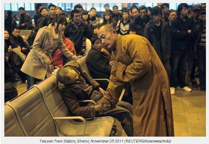 A monk prays for a dead man in the station hall of the Shanxi Taiyuan Train Station, China. The man died suddenly of natural causes while waiting for a train.
