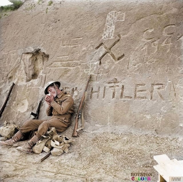 An Allied Soldier takes a break during the approach to Tripoli, Libya beside a swastika and the words 'Heil Hitler' that have been carved into a rocky hillside during January 1943. (Source - © IWM E 21788. Colorized by Royston Leonard from the UK)
