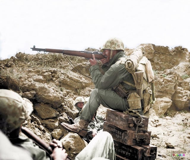 An American Marine aiming his Garand M1 rifle, whilst perched on Japanese ammunition crates on the Island of Iwo Jima, c. February/March 1945. (Colourised by Royston Leonard from the UK)