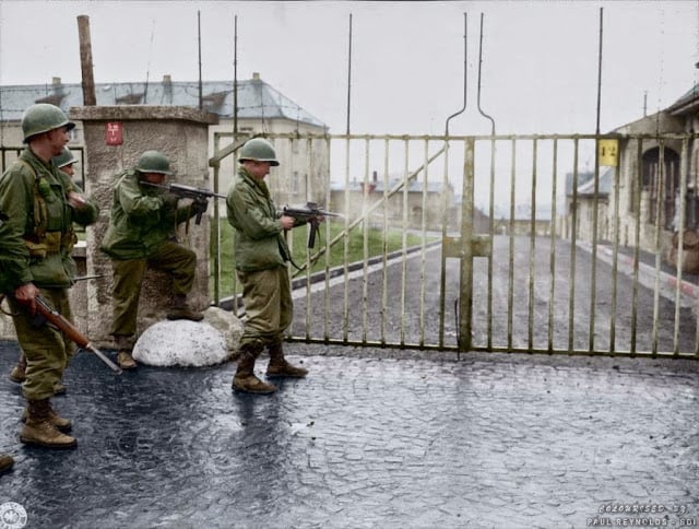US troops from Combat Command B of the U.S. 14th Armored Division entering the Hammelburg Prison in Germany by opening the main gate with bursts of their M3 "Grease Guns". Hammelburg, Germany. April 6, 1945. (Colorized by Paul Reynolds. Historic Military Photo Colourisations)