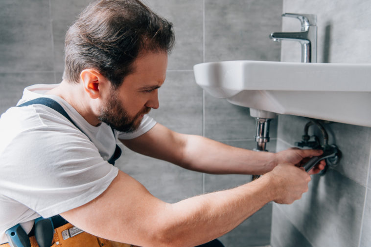 adult male plumber in working overall fixing sink XNPAWTE