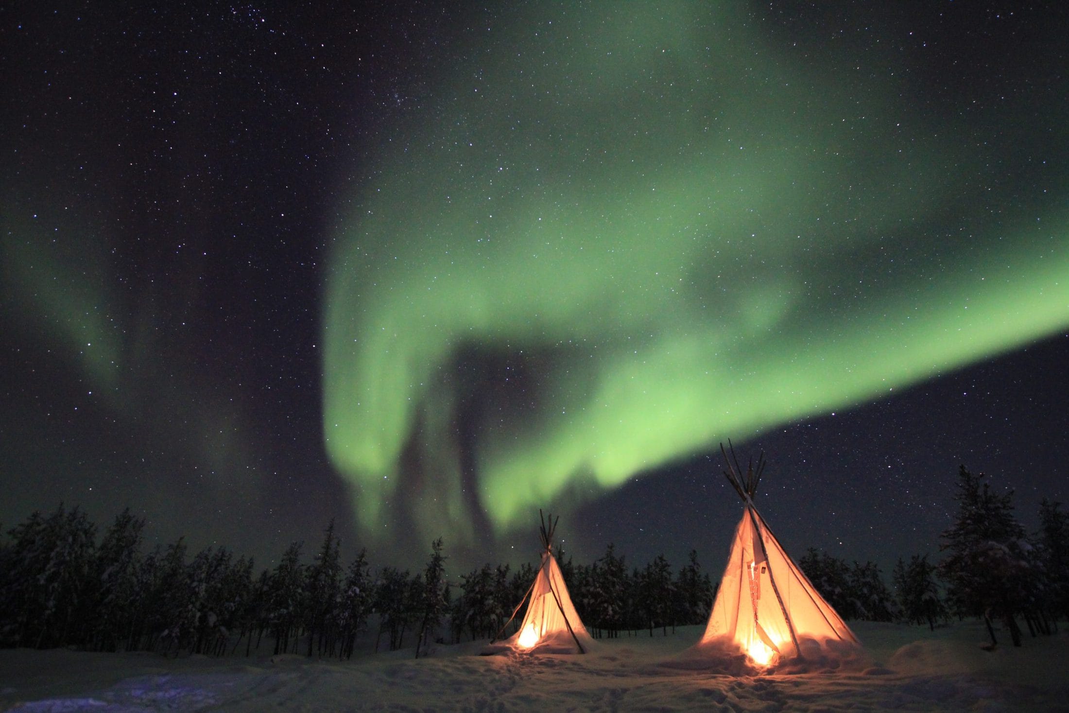 The top places to photograph the Northern Lights lighted tipi tent under green northern lights