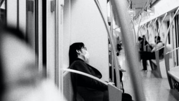 grayscale photo of woman in black jacket sitting on train