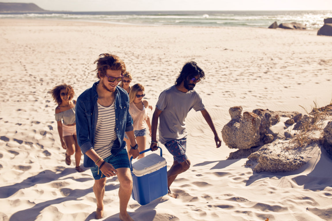 group of friends carrying cooler to party on beach P6CGPJK