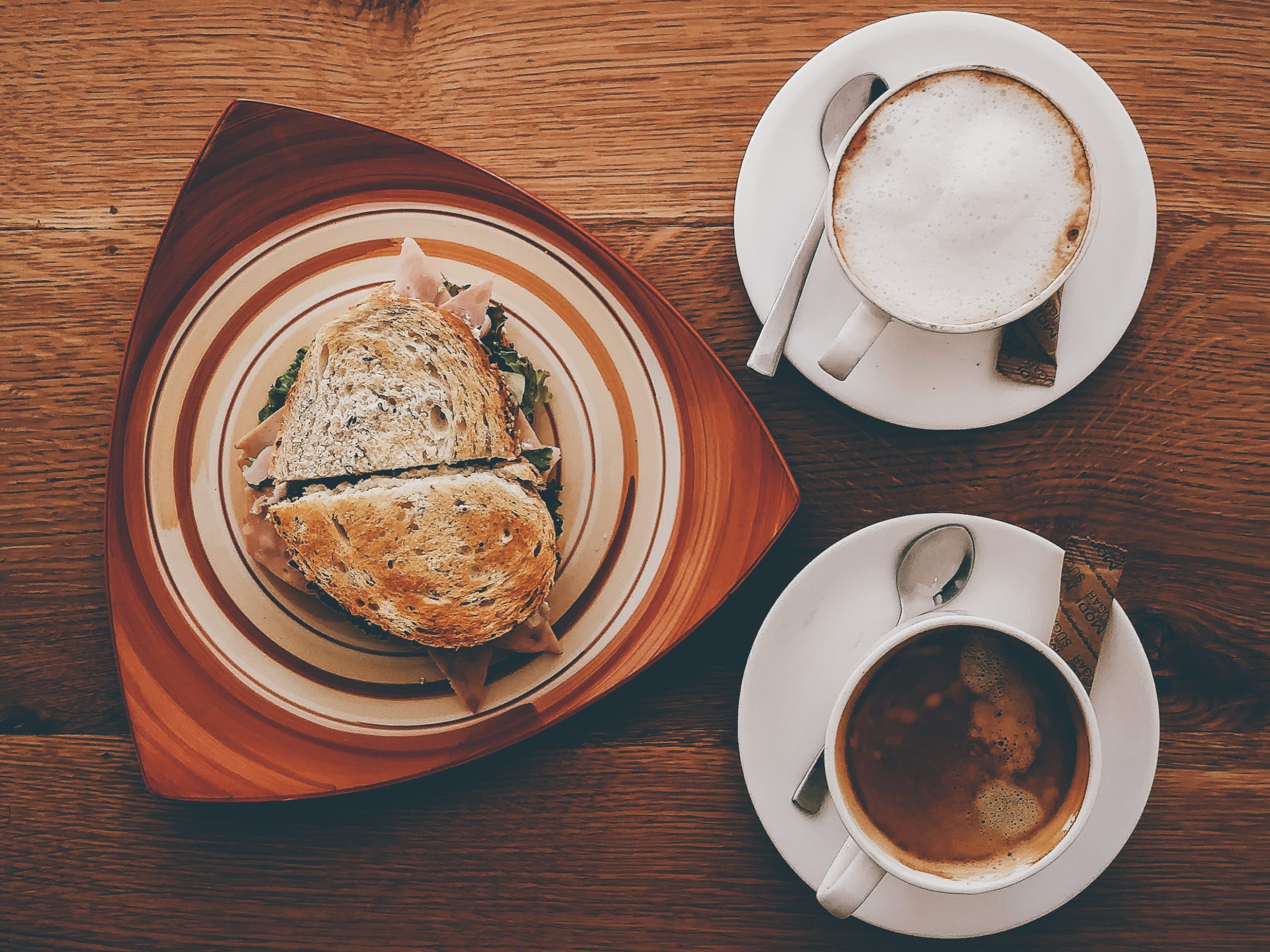 ham sandwich on plate near cappuccino on mug and coffee