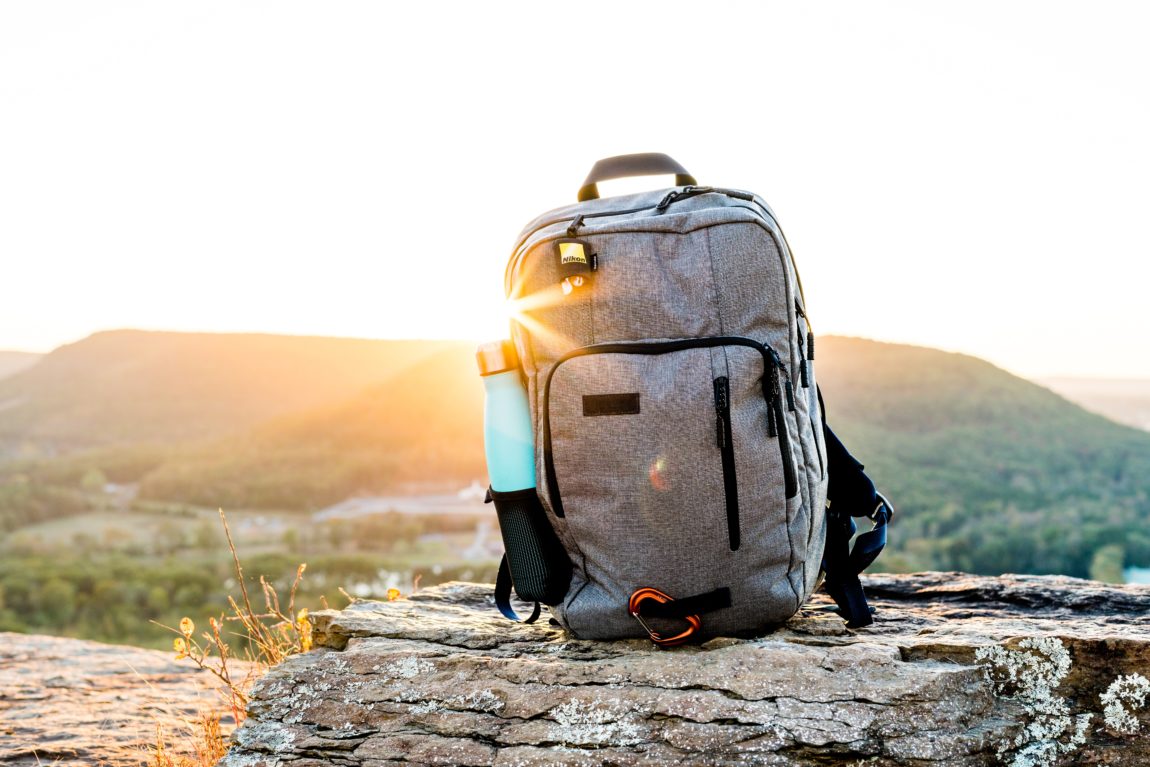Backpack grey and black hiking backpack and cyan tumbler on grey rock during sunset