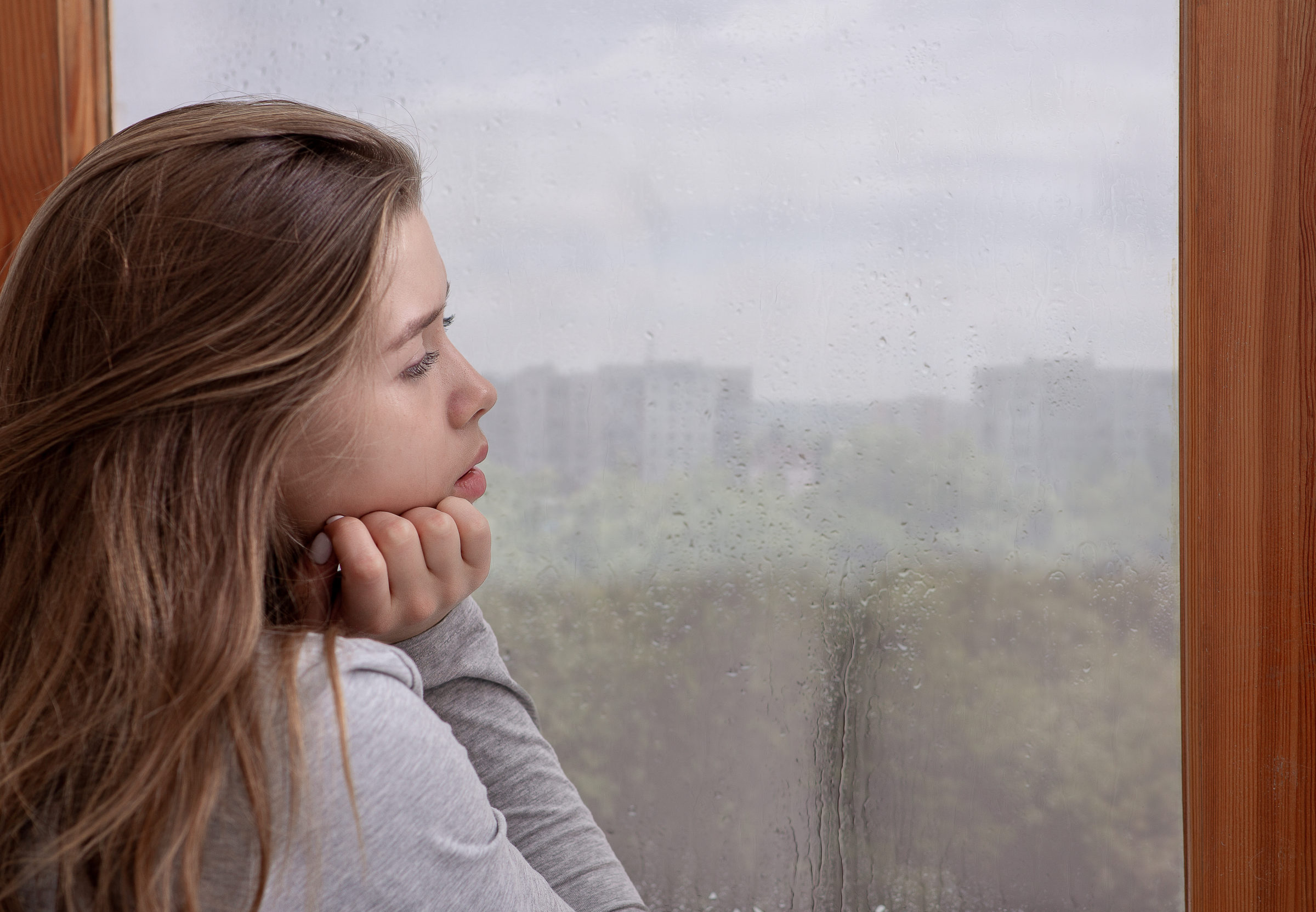 sad young woman looking out window lost in thought DWFZ334