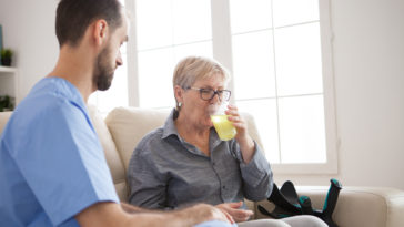young caregiver sitting down on couch with senior QTNBSQF