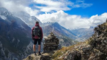 man standing on top of mountain beside cairn stones