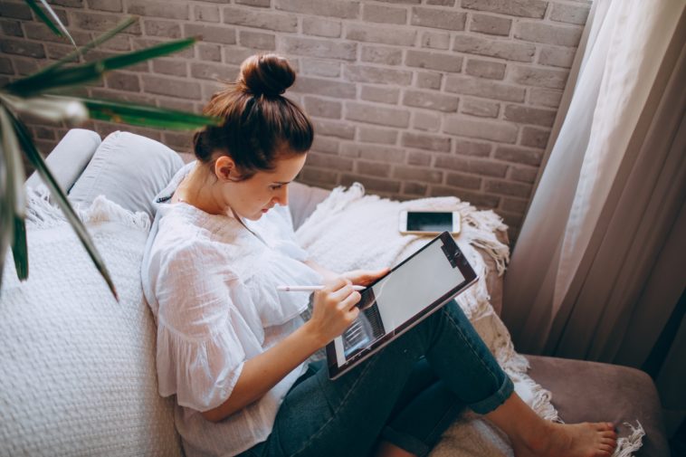 Creative director woman in white shirt and blue denim jeans sitting on gray couch