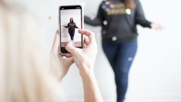 person holding white smartphone taking photo of woman wearing blue jeans