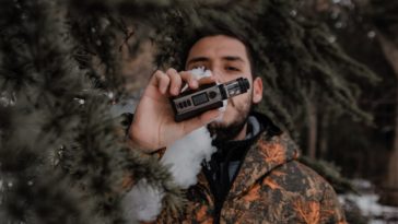 man in brown and black camouflage jacket holding black and silver camera
