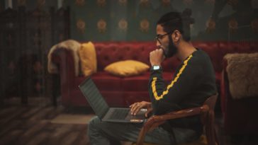 man sitting on wooden chair while using laptop computer on lap