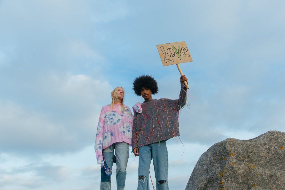 man and woman standing near a boulder while holding a love signage