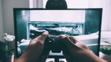 person holding game controller in-front of television