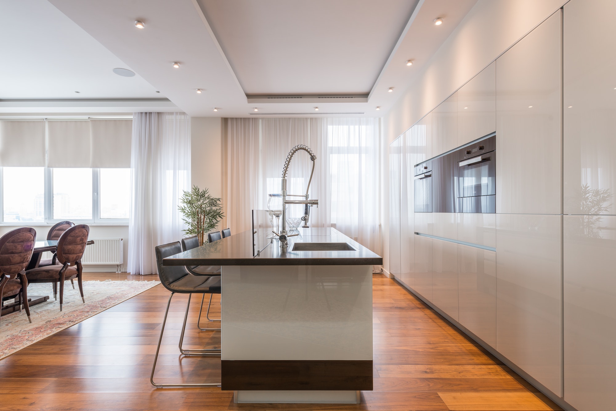 Interior of spacious kitchen with modern minimalist furniture with built in appliances and dining zone in contemporary apartment in daylight