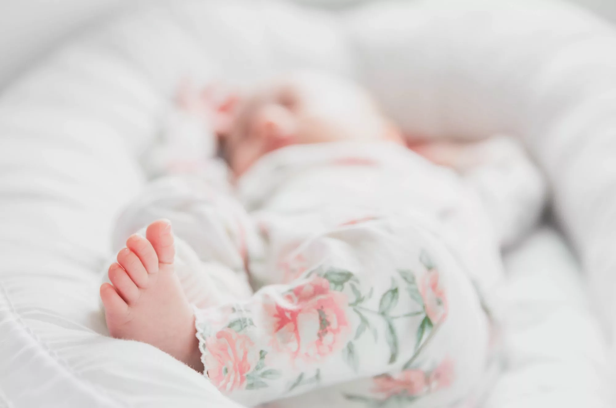 baby in white and red floral onesie lying on bed