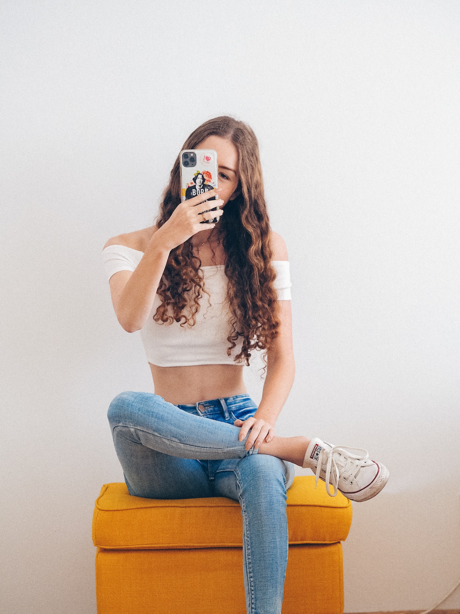 woman in white crop top and blue denim jeans sitting on brown wooden seat